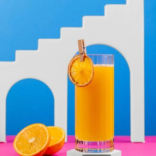 A glass of orange juice with two half-cut oranges on the side 