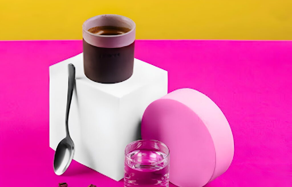 A glass with espresso, along with a glass of water and spoon on a stand