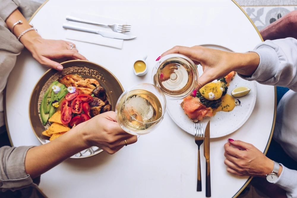 Friends enjoying a stylish brunch at Trove Restaurant Dubai, featuring vibrant dishes like avocado salad and smoked salmon eggs benedict, paired with glasses of white wine.