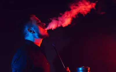 Man enjoying shisha, exhaling vibrant red smoke in a dark, artistic setting that reflects a luxury shisha experience in Dubai.