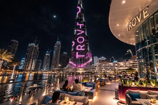 Diners on the Trove terrace at night with the Burj Khalifa and the Downtown Dubai skyline across Burj Lake
