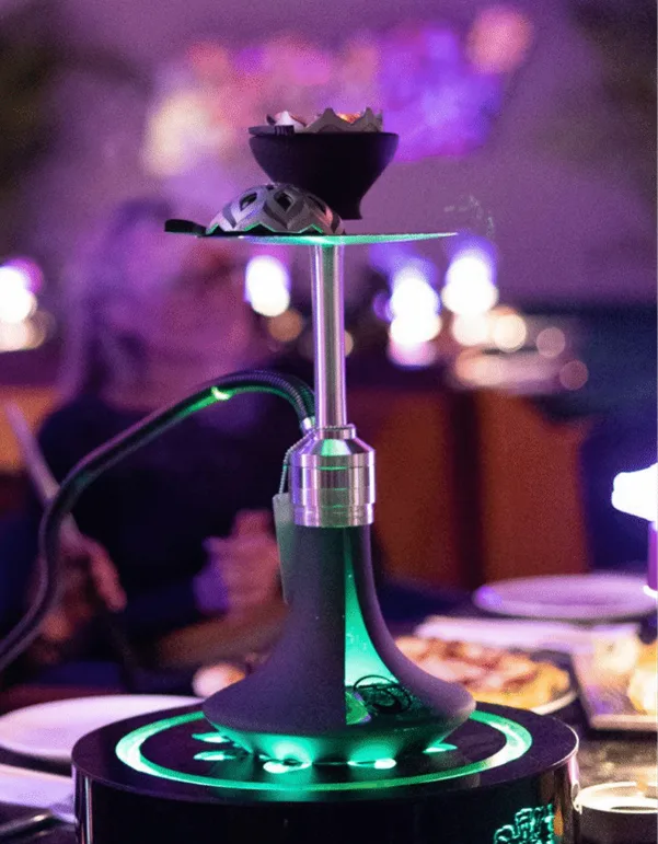 Close-up of a modern illuminated shisha with green lighting on a table set at a shisha lounge in Dubai