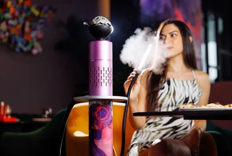 Woman enjoying shisha seated beside a vibrant hookah with food on the table