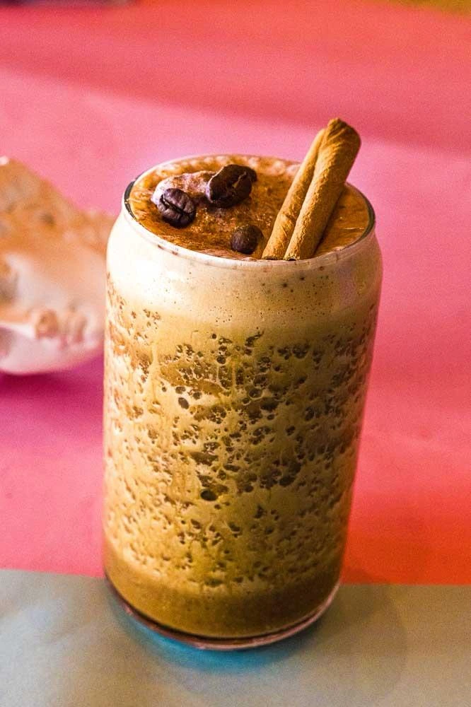 A glass of coffee smoothie with coffee beans on the top 