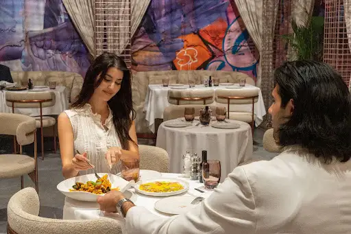 Couple sharing a private dining table at Trove in Dubai Mall, with seafood pasta and street art behind them